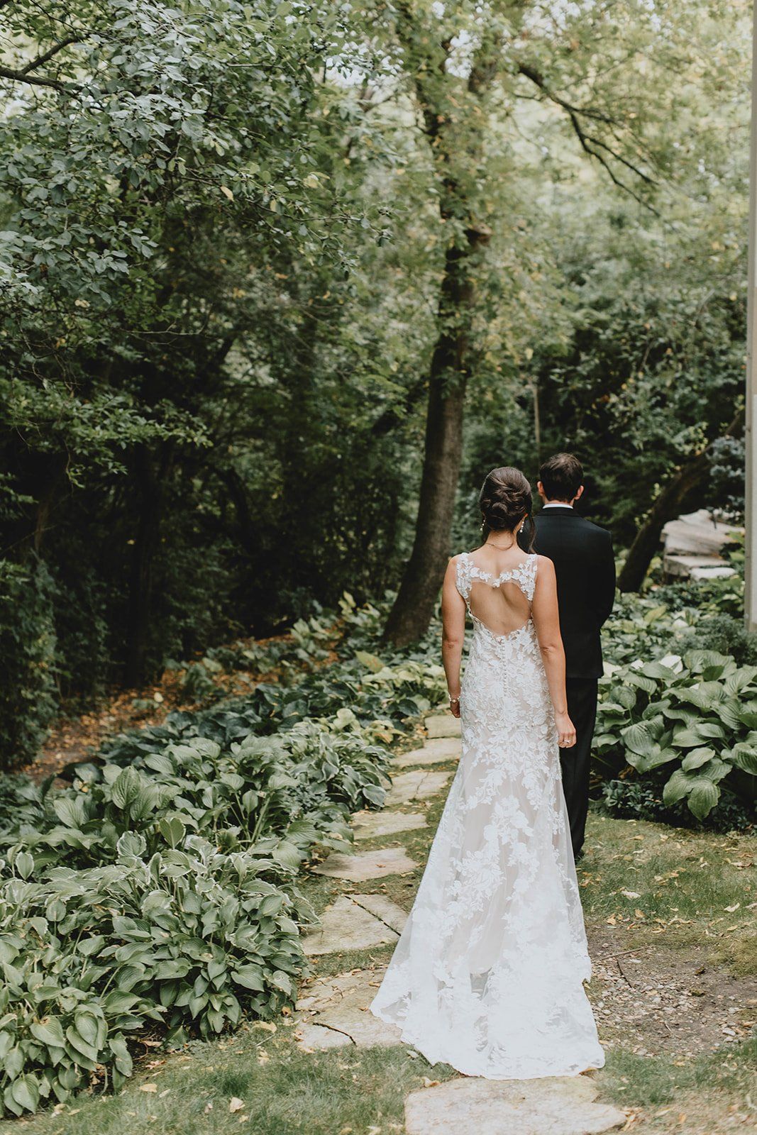 A bride and groom are walking down a path in the woods.