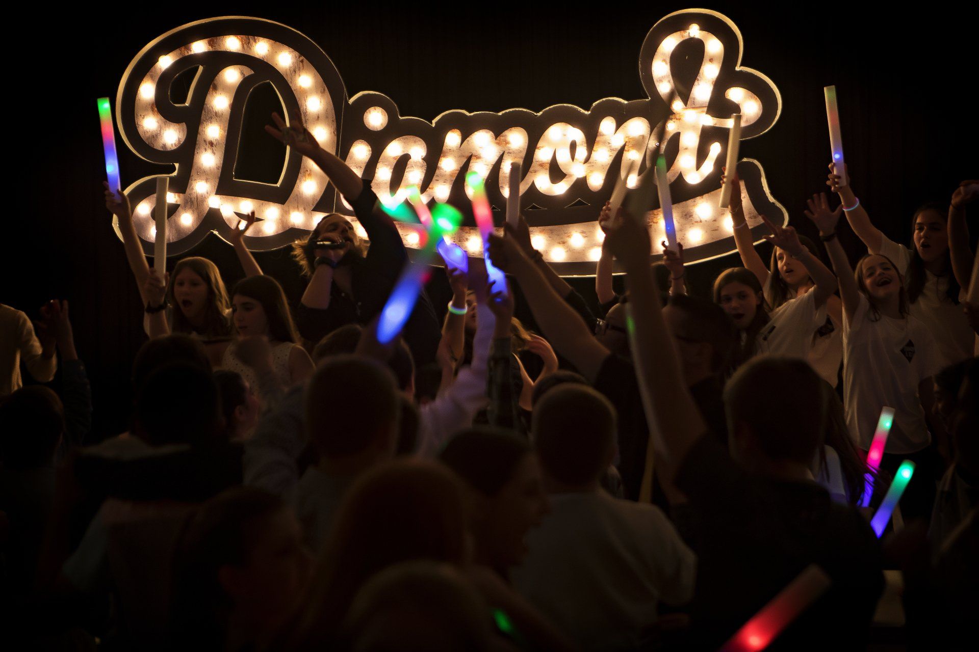 A crowd of people holding glow sticks in front of a diamond sign