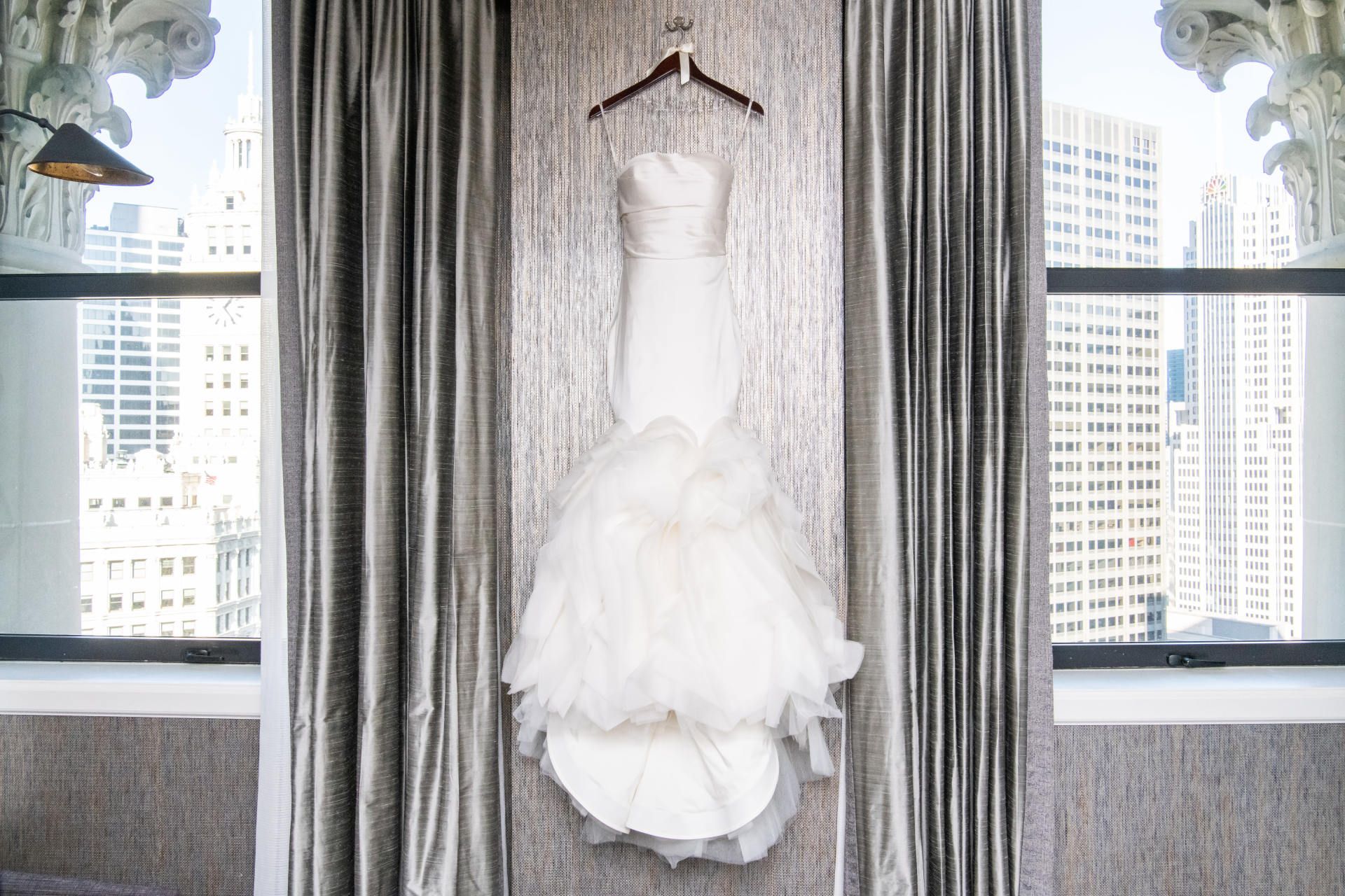 A wedding dress is hanging on a hanger in front of a window.