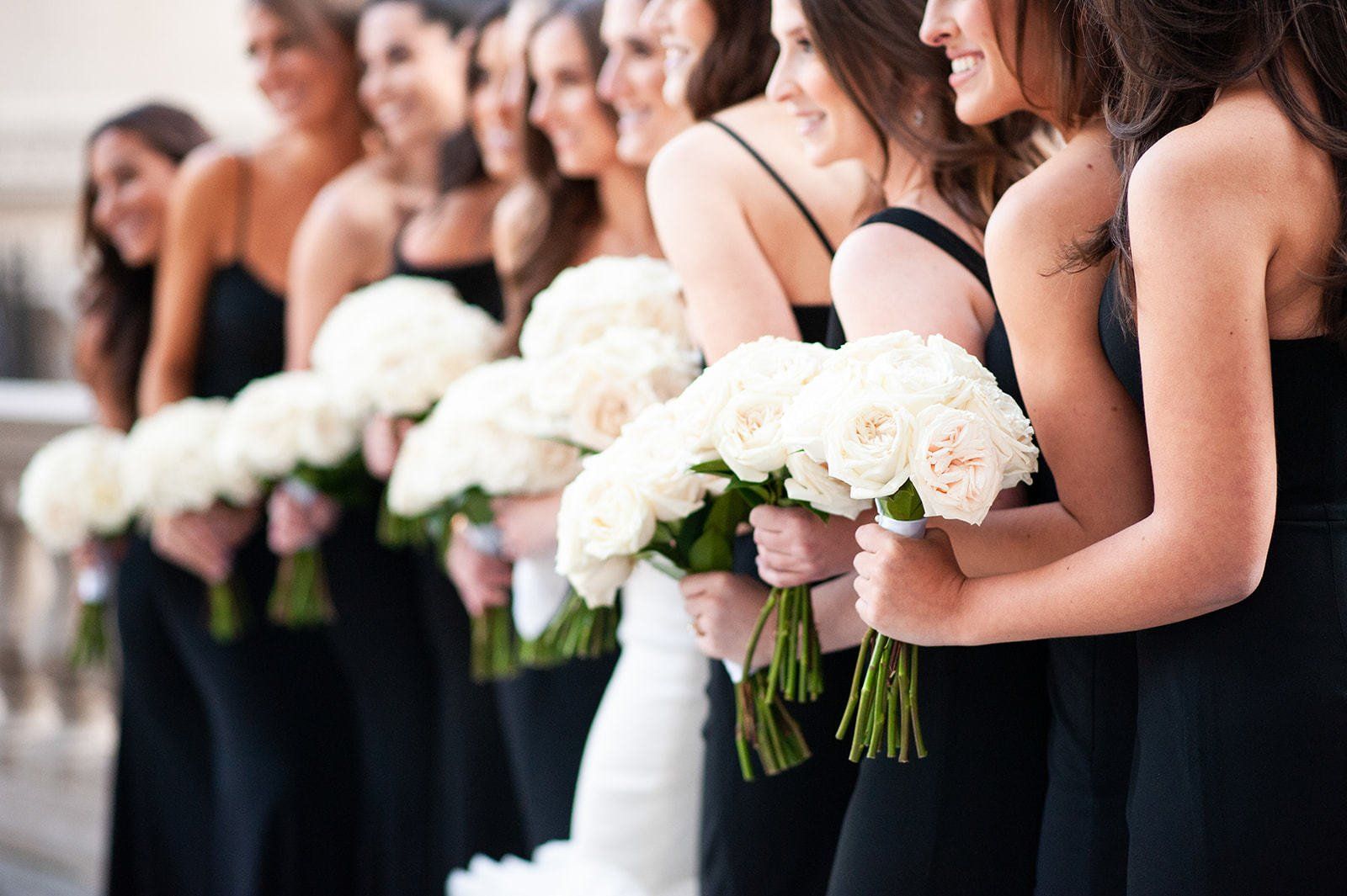 The bride and her bridesmaids are wearing black dresses and holding white flowers