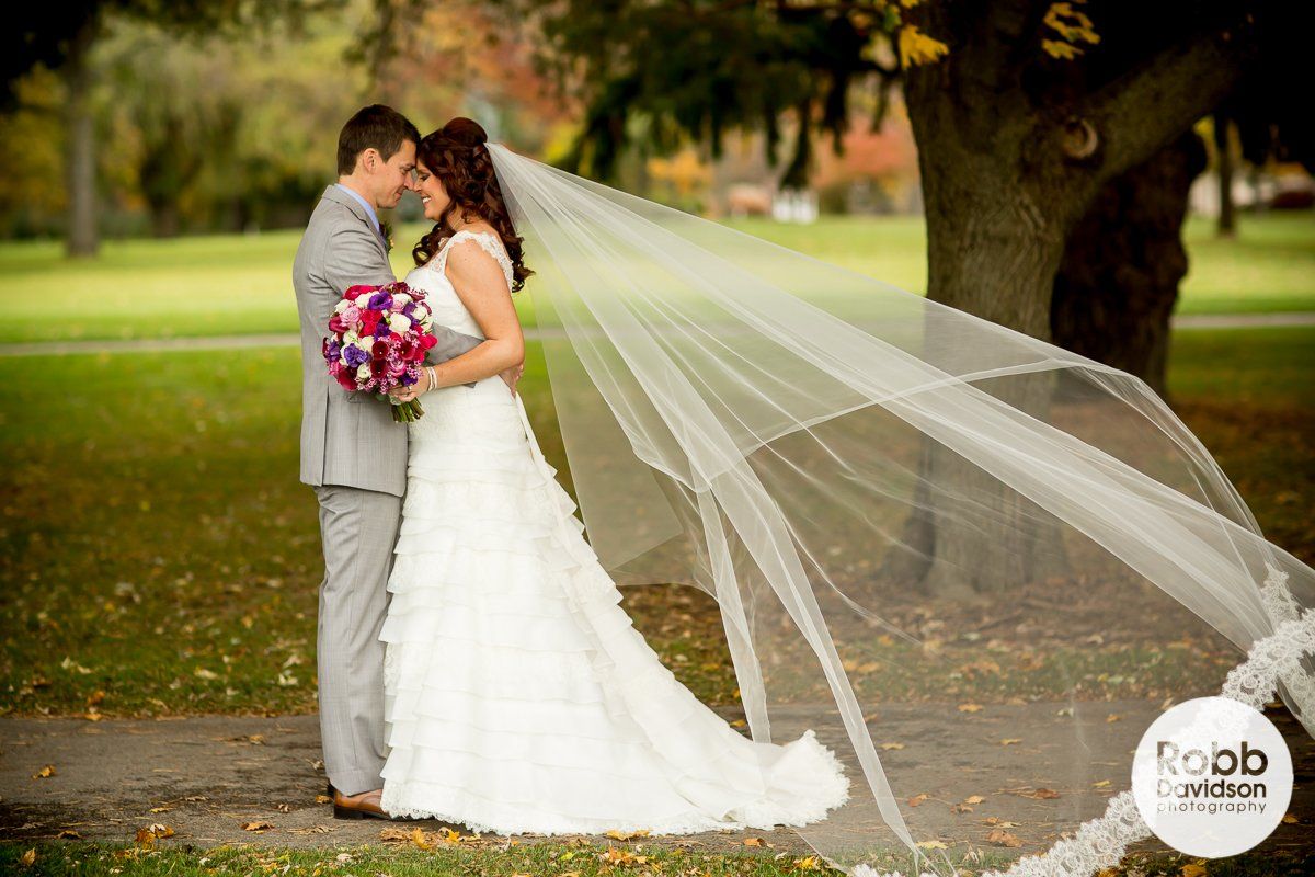 A bride and groom are posing for a picture with their veil blowing in the wind