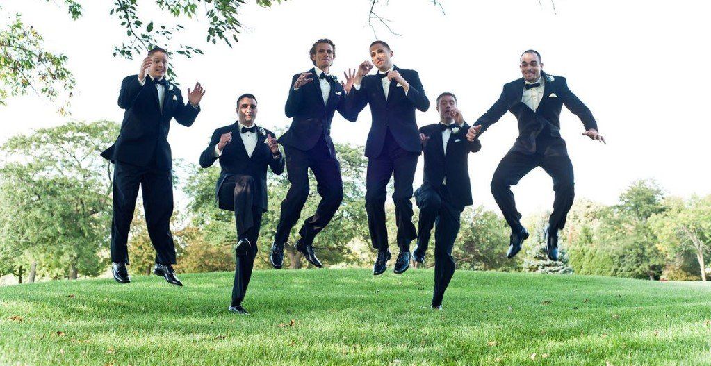 A group of men in tuxedos are jumping in the air.