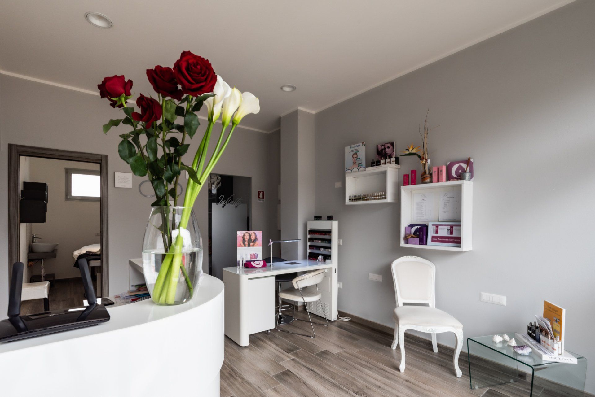Un salone dben illuminato con una reception , un vaso di fiori, una postazione per la manicure e sedie nella zona d'attesa.