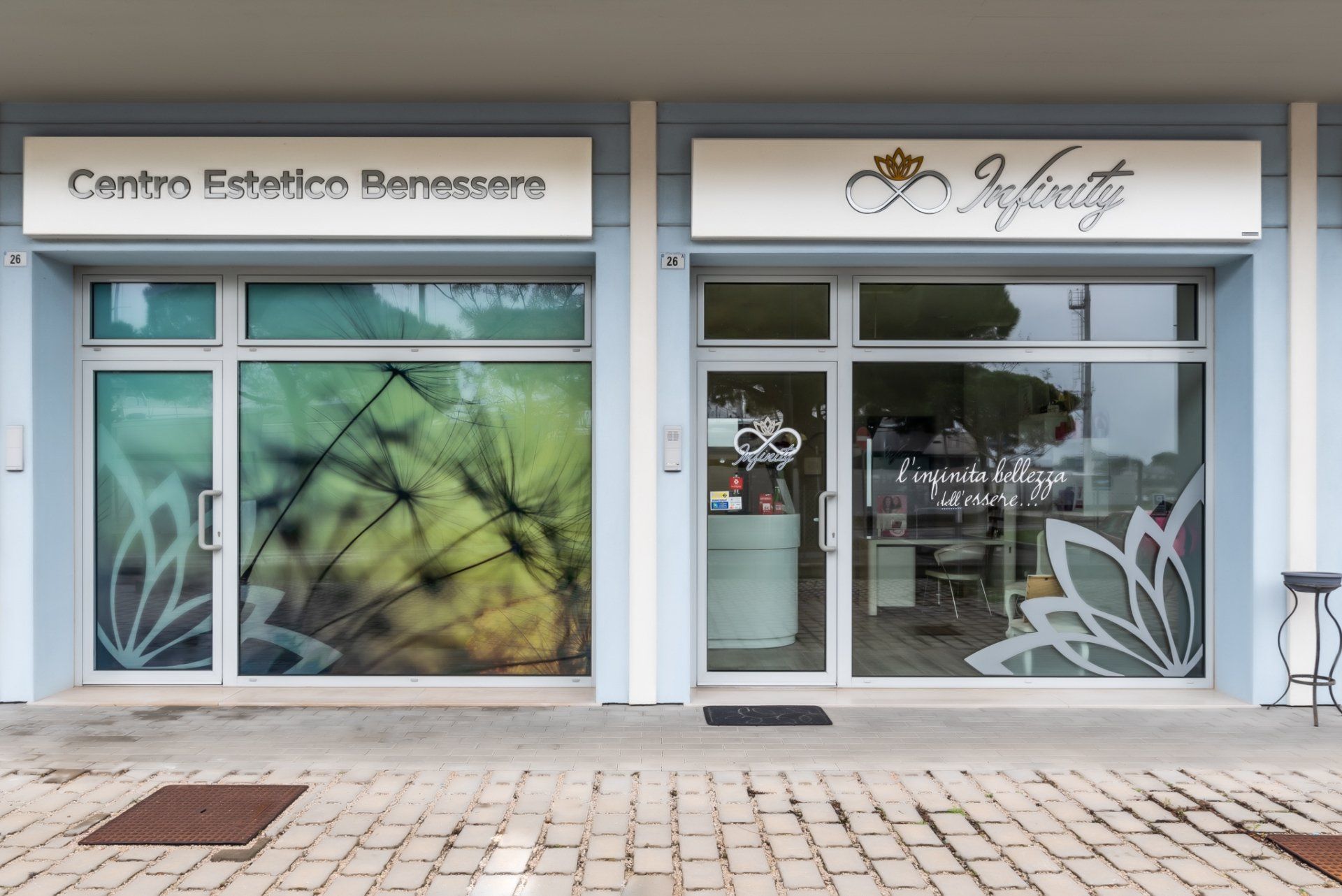 La vetrina del Centro Estetico Benessere Infinity, con ampie finestre e decorazioni floreali su un marciapiede pavimentato.