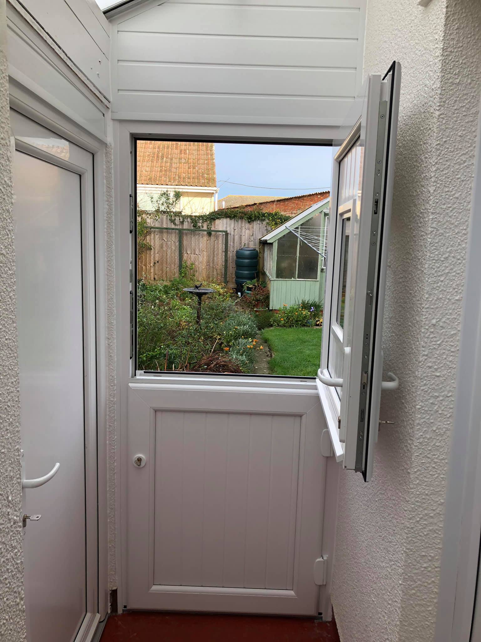 A white door with an open window leading to a garden.