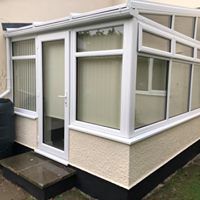 A white conservatory with a door and windows on the side of a house.
