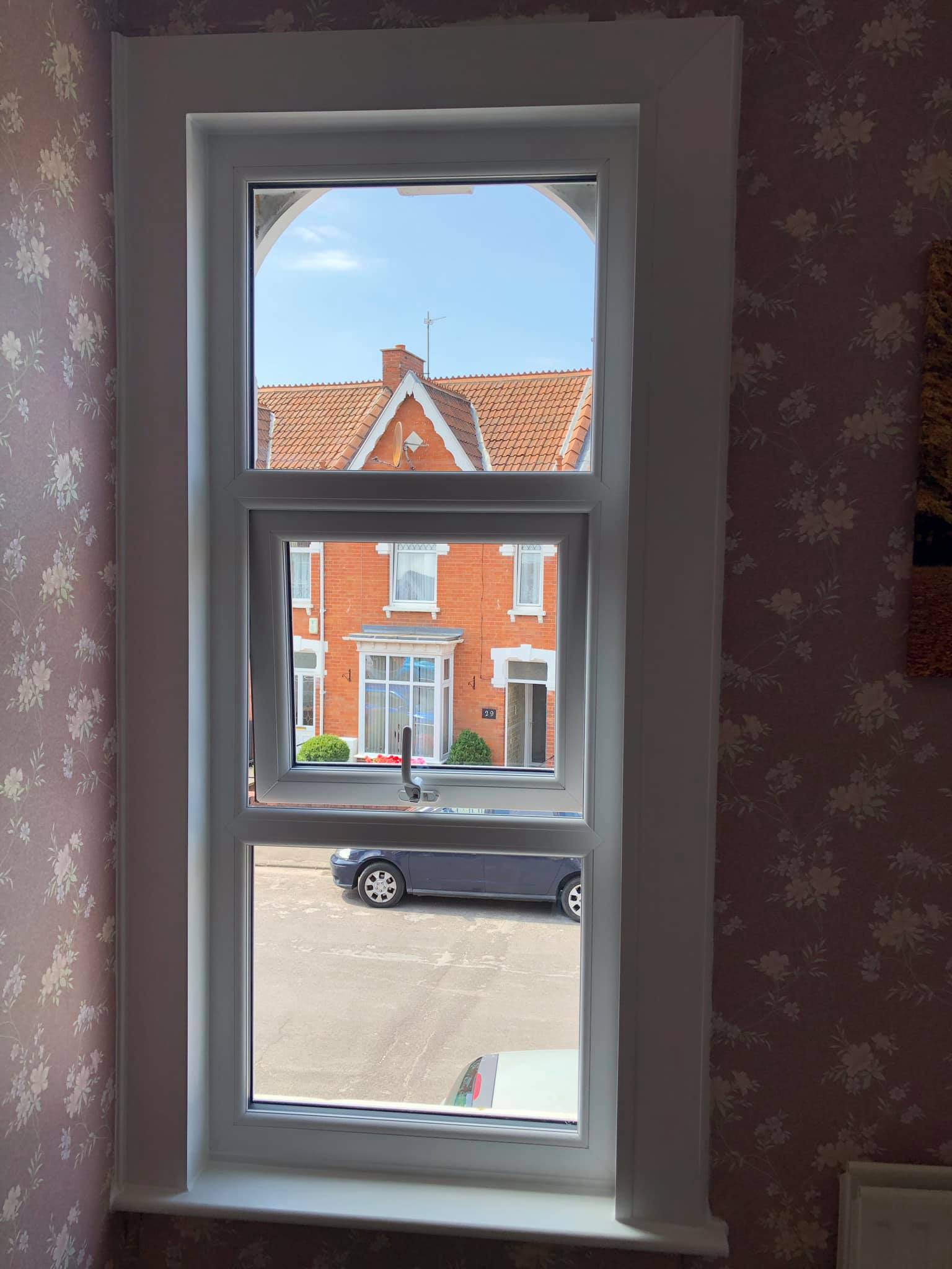 A window with a view of a brick house and a car parked in front of it.