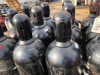 Black industrial gas cylinders, outdoors, clustered together.
