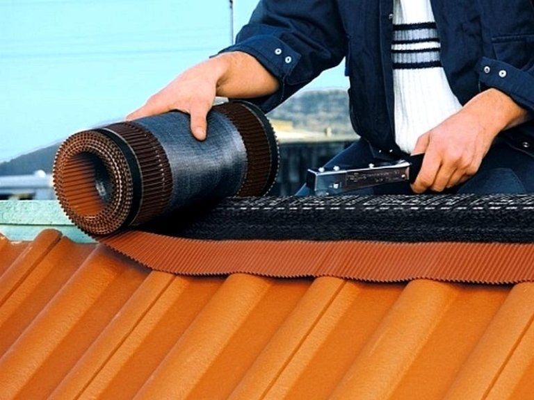 Persona che installa un rivestimento in lamiera su un tetto di tegole arancioni.