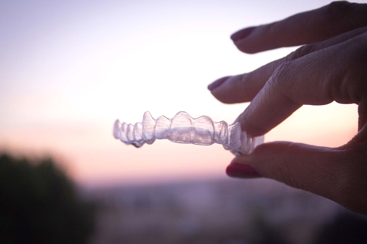 A woman is holding a clear retainer in her hand.
