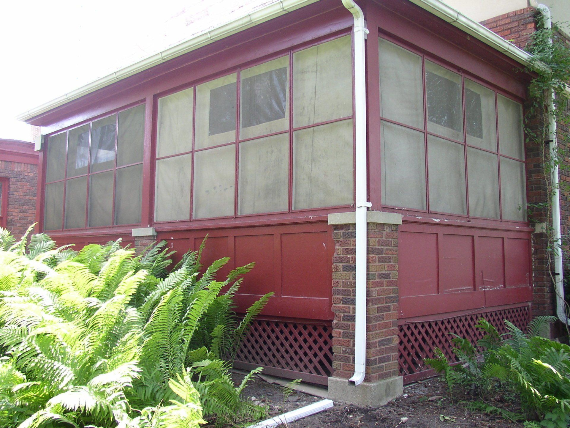 A red screened in porch is surrounded by ferns