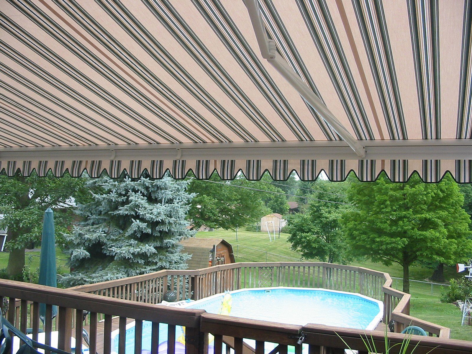 A deck with a swimming pool under a striped awning
