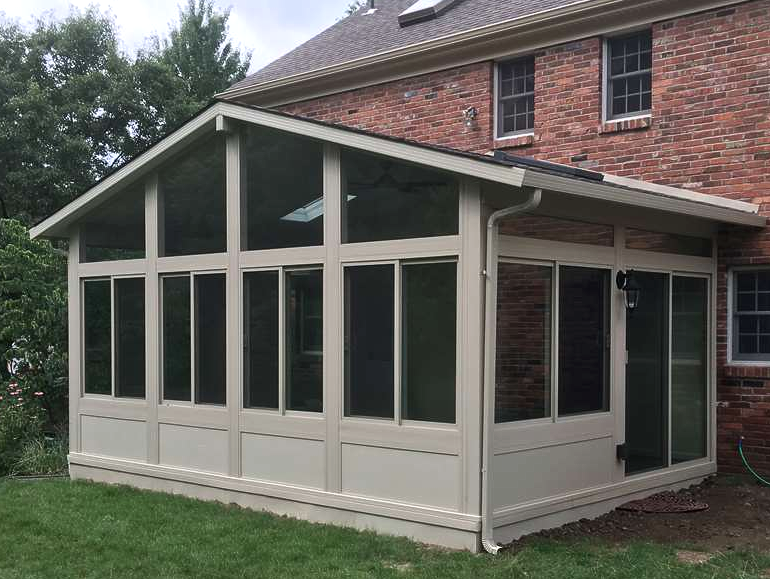 A sun room is attached to the side of a brick house.