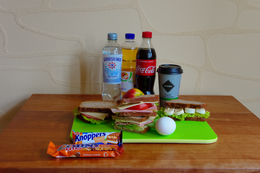 Mittagsbuffet: Sandwiches, Getränke, Snacks und Ei auf einem grünen Schneidebrett, angerichtet auf einem Holztisch.