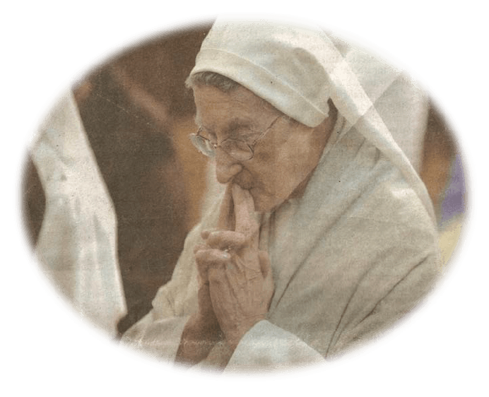 An older woman wearing glasses and a white robe is praying