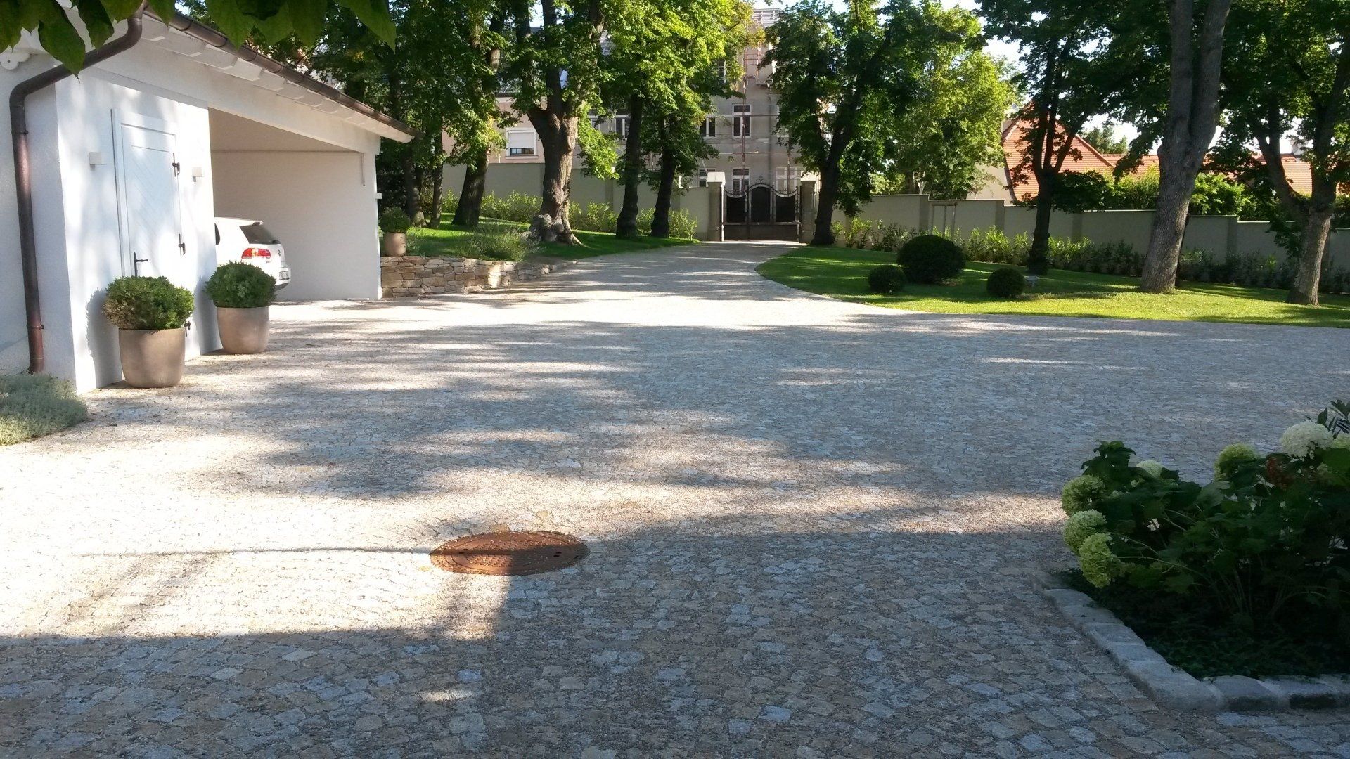 Sonnendurchfluteter Kopfsteinpflasterhof mit Bäumen, einem weißen Gebäude und Topfpflanzen