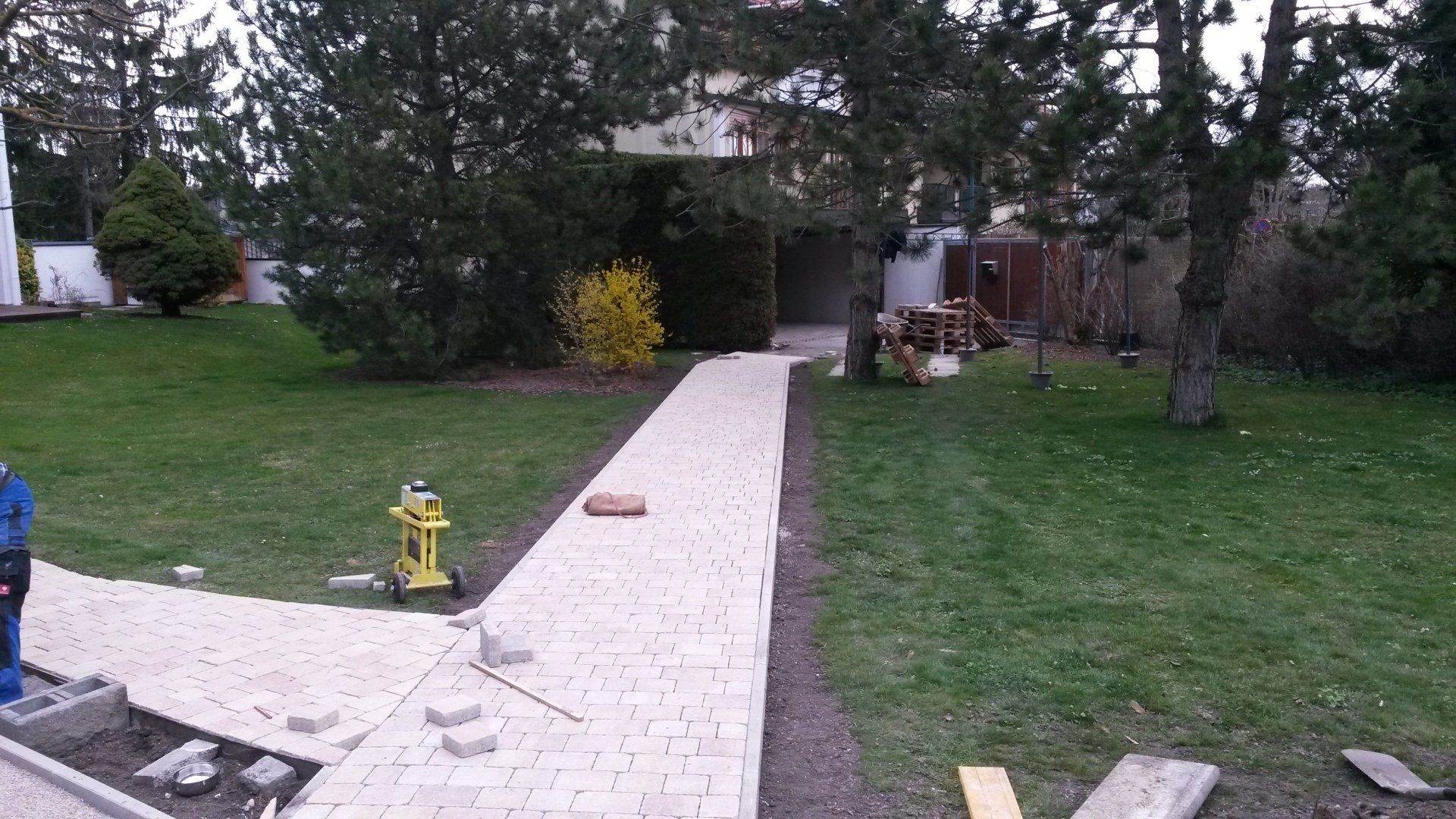 Hinterhof mit einem weißen Gehweg, der zu einem Haus führt, umgeben von Rasen und Bäumen, mit einem gelben Hydranten in der Nähe