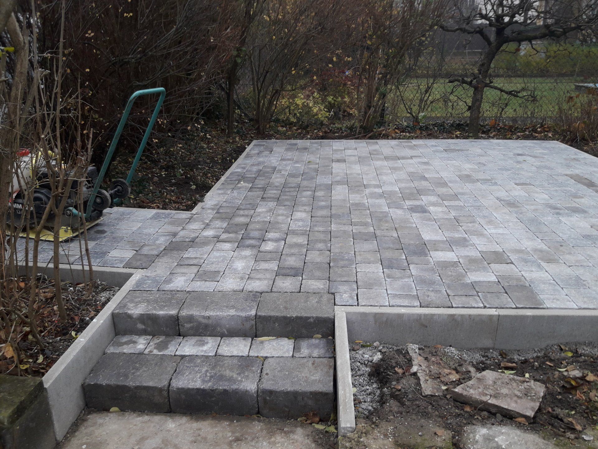 Gepflasterte Terrasse im Hinterhof mit grauen Steinstufen, eingefasst von einer Betoneinfassung und Gartenbeeten