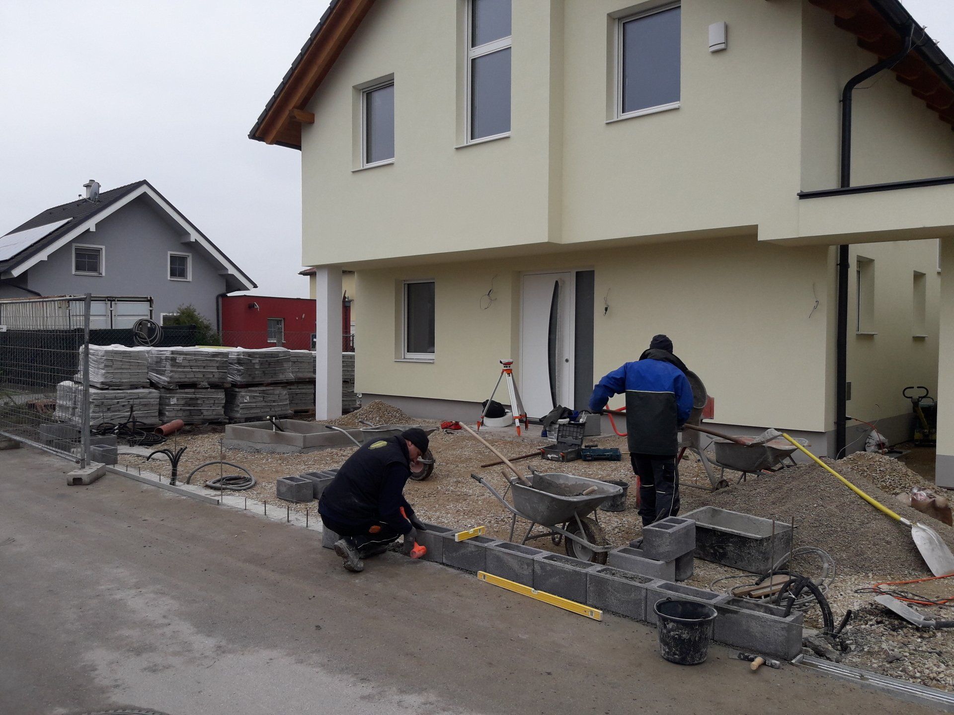 Arbeiter verlegen Pflastersteine ​​neben einem cremefarbenen Haus in einer im Bau befindlichen Wohnstraße.
