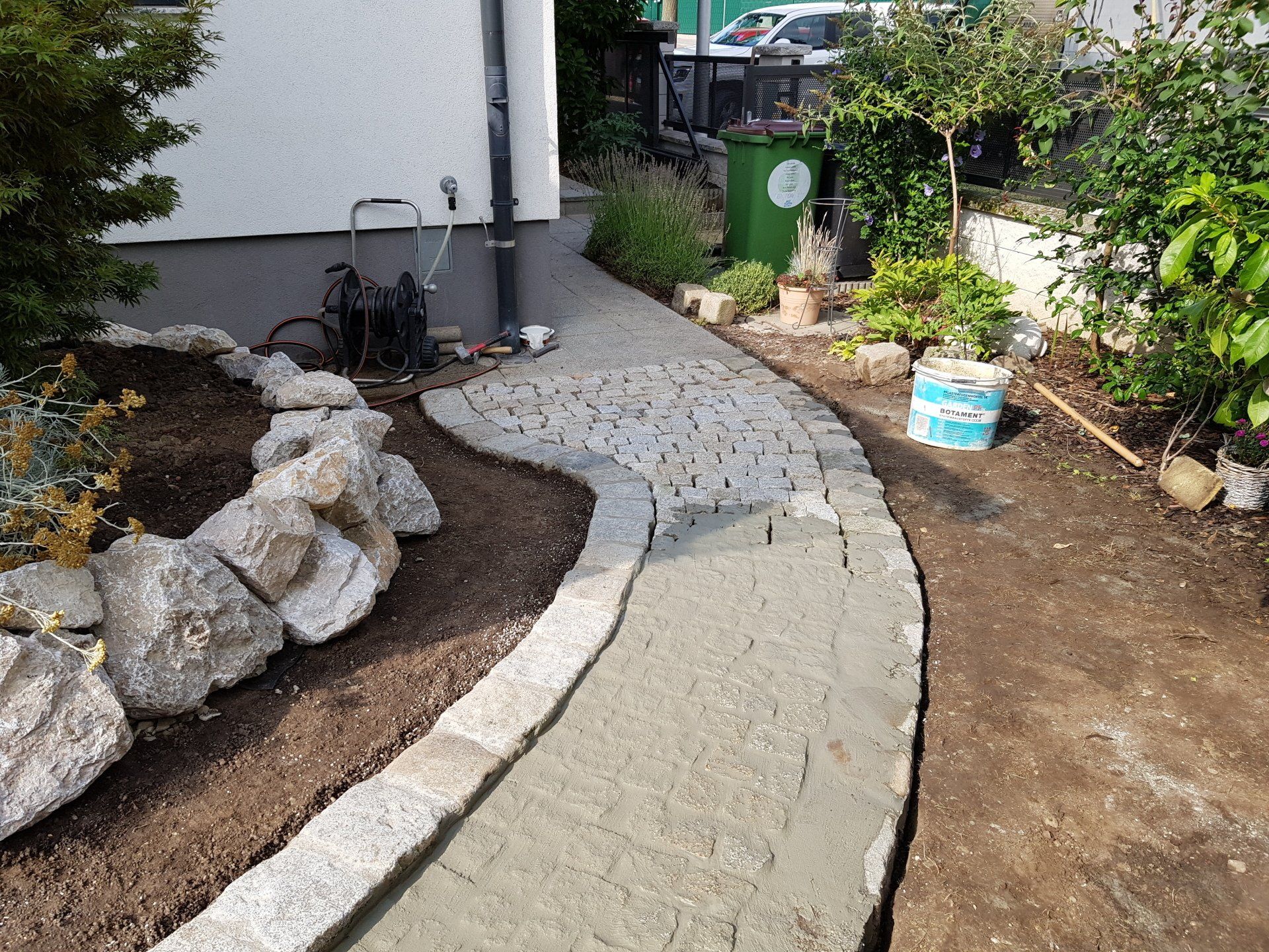 Geschwungener Steingartenweg neben einem Haus, mit Steinen, Mulch und Pflanzen am Rand