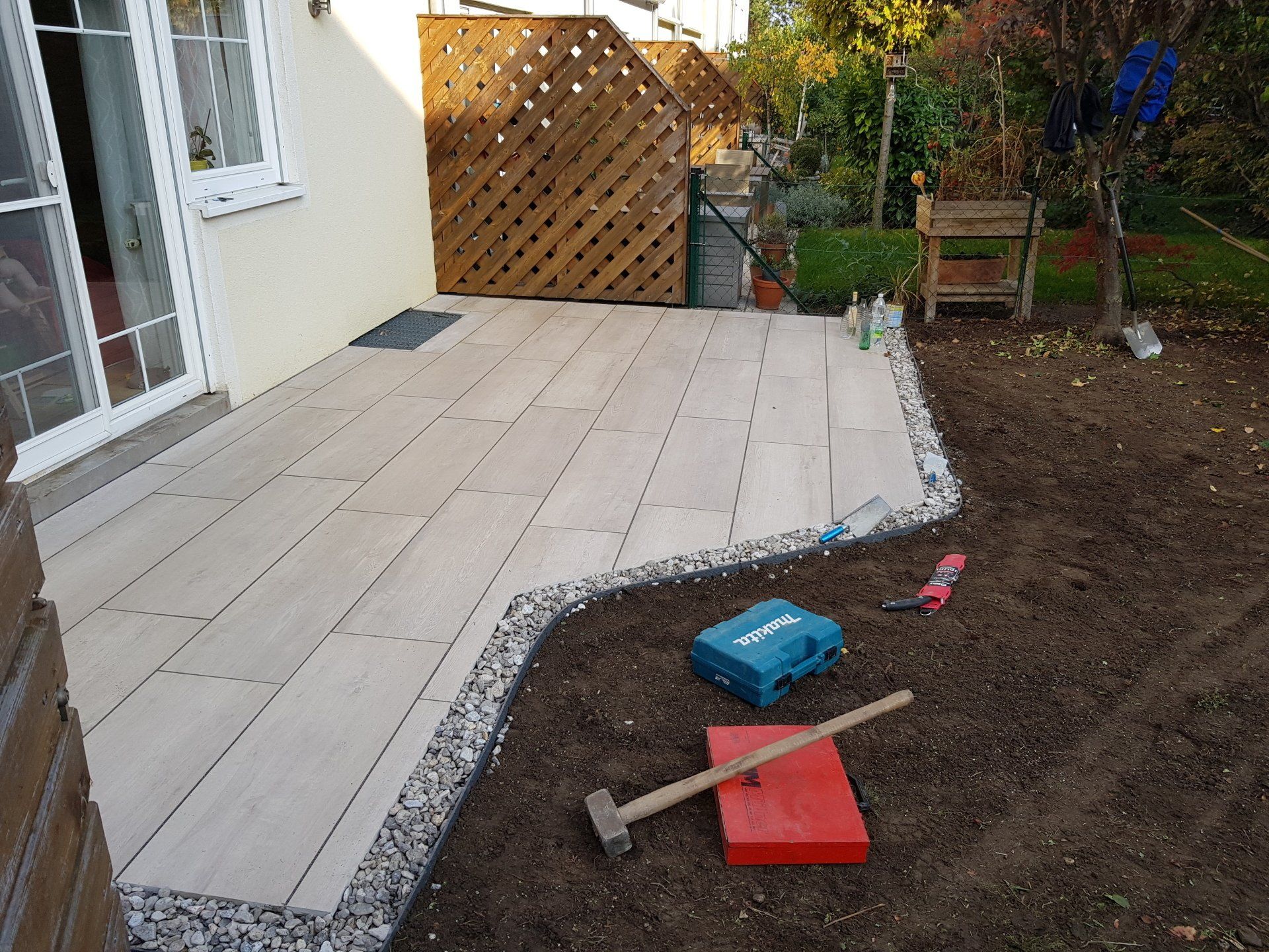 Die Terrasse im Hinterhof befindet sich im Bau und besteht aus beigen Pflastersteinen, einem Erdrand und Werkzeugen auf dem Boden.