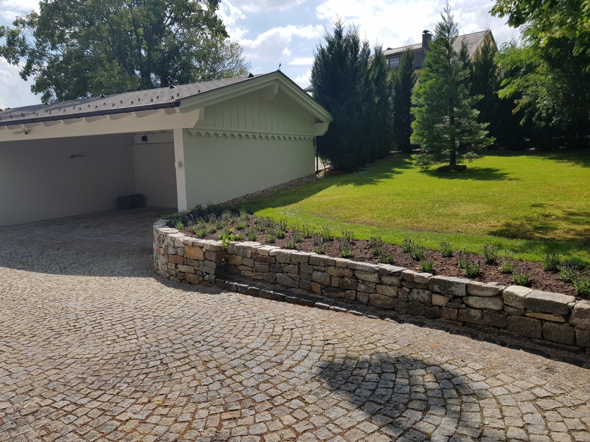 Steinauffahrt neben einer grünen Garage und einem gepflegten Rasen unter sonnigem Himmel