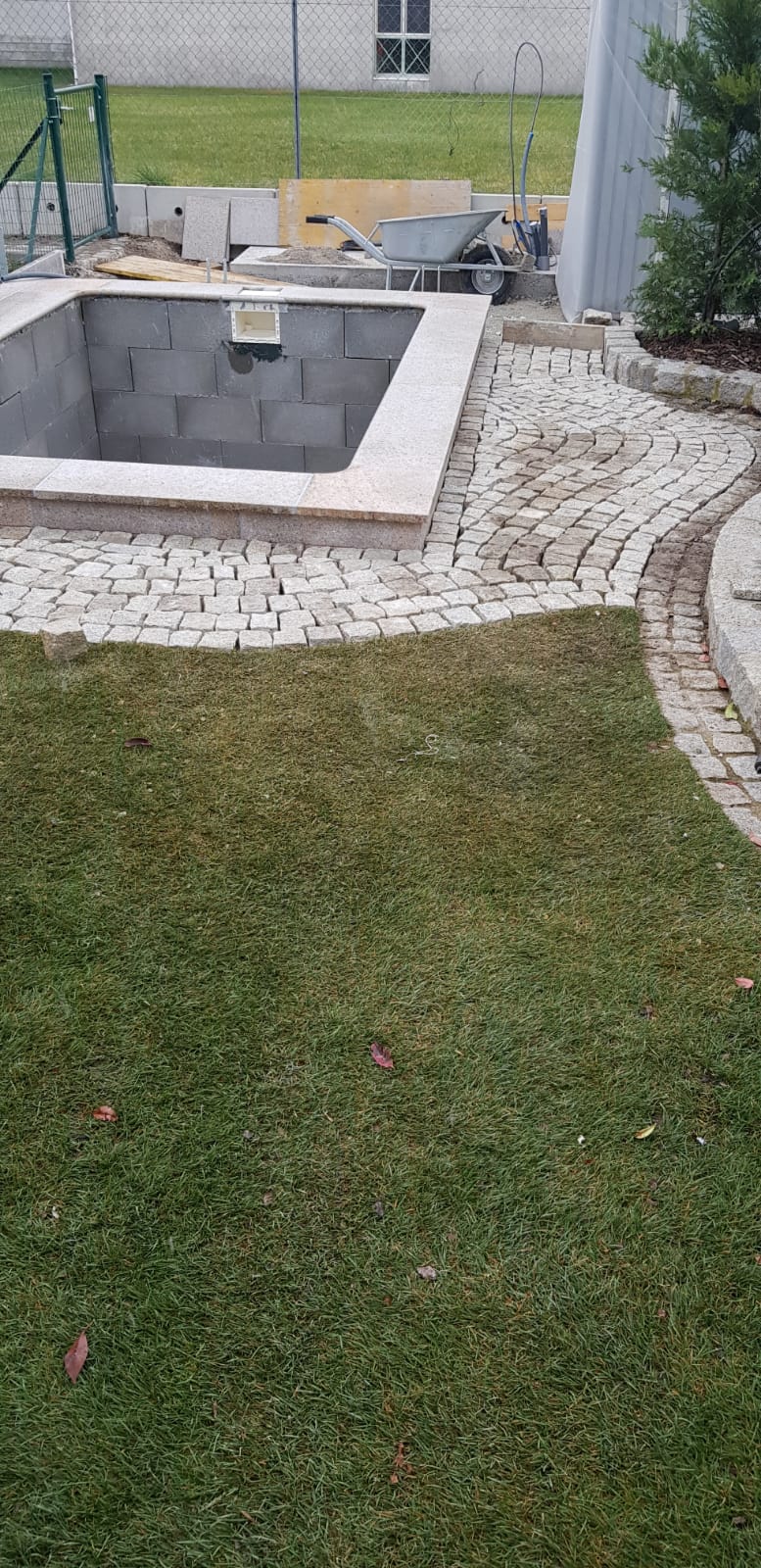 Hinterhof mit einem mit Steinen ausgekleideten Whirlpool neben einem Rasen und einer umzäunten Terrassenfläche