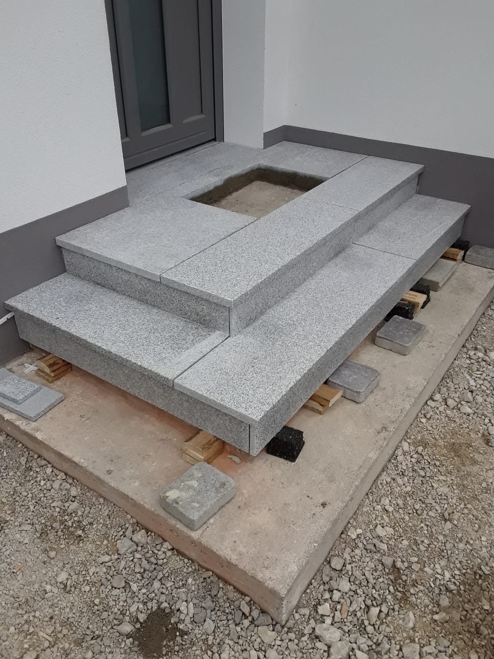 Eine graue Granitstufenplattform steht auf einem Betonsockel neben einem Gebäudeeingang.
