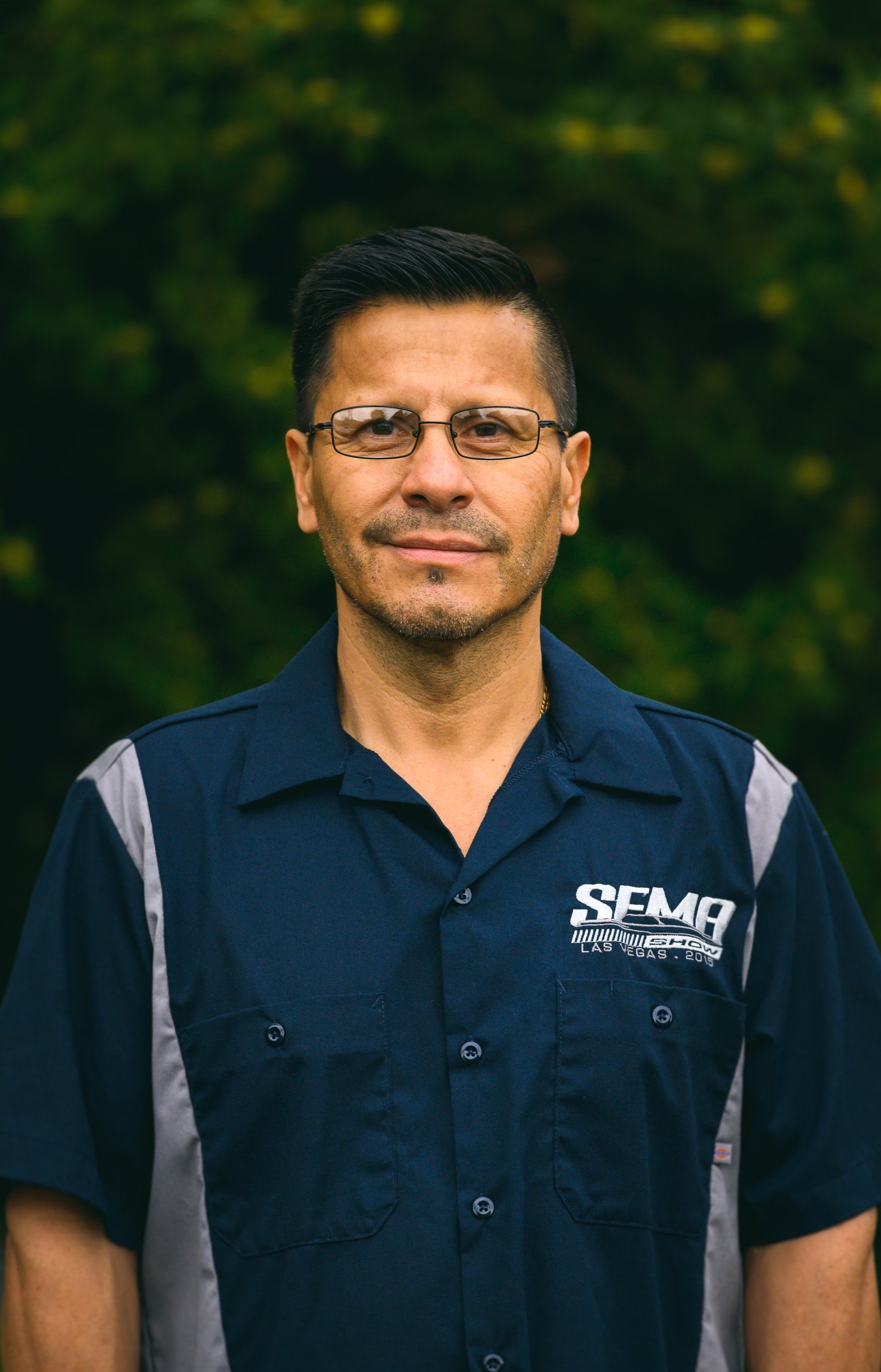 Man in glasses and blue work shirt, standing outdoors with a neutral expression.