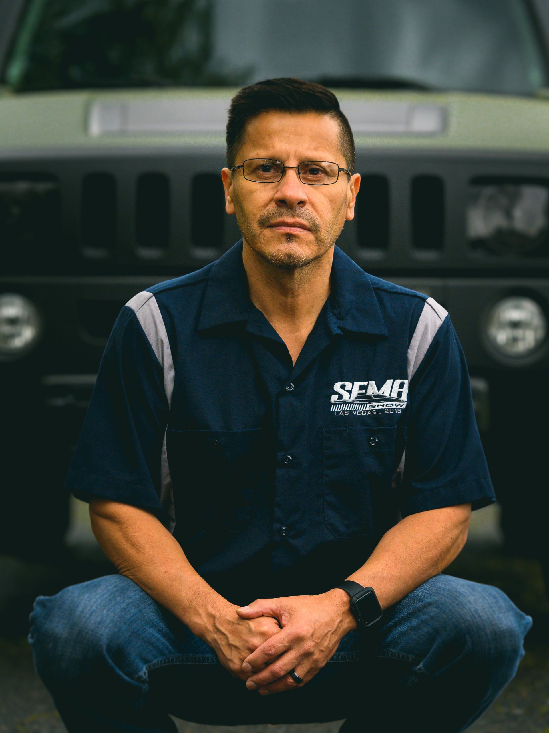 Man in work shirt squats in front of a Hummer.