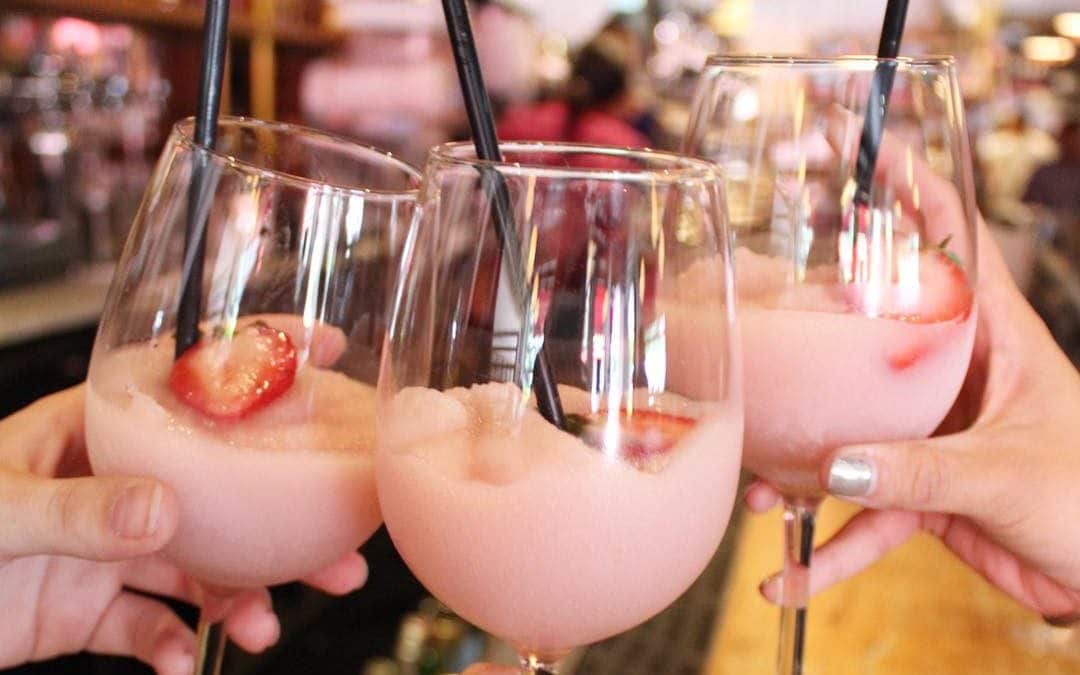 Three people are holding pink drinks with straws in them.