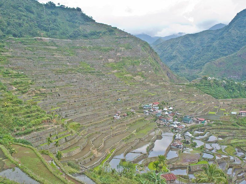 A view of a village in the middle of a valley surrounded by mountains.