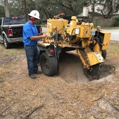 A man wearing a hard hat is working on a tree stump grinder