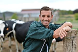 Man farmer leaning against a post with livestock in the background - livestock insurance