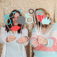 Two women are holding paper props in front of their faces.