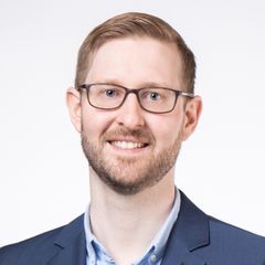 Tobias Meyer, short blonde hair, glasses and 5 day beard dressed in a blue suit with light blue shirt