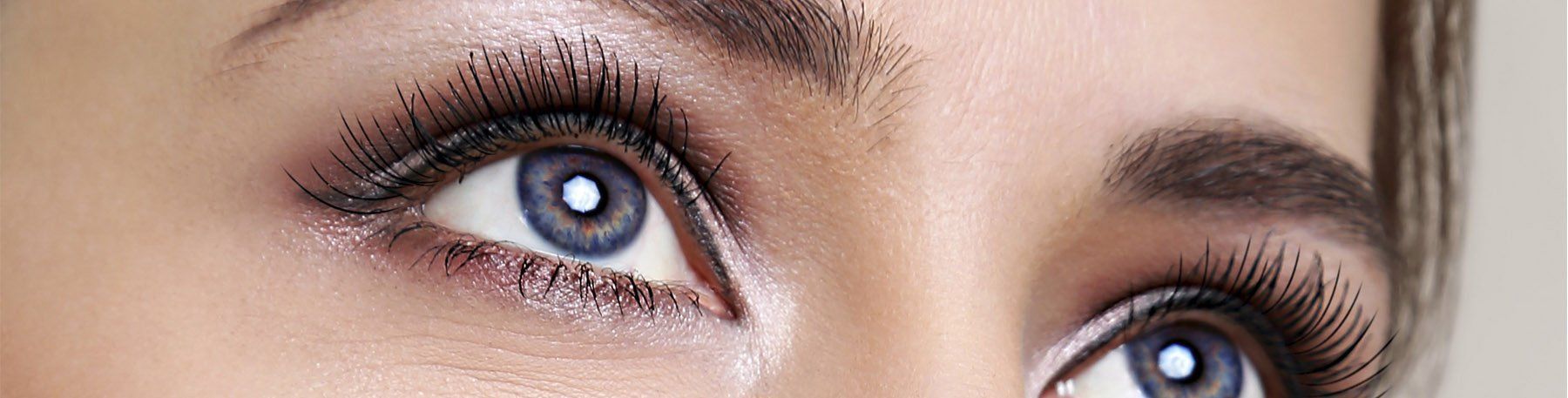 Close-up of a person's eyes, light blue irises, dark eyelashes and eyebrows, wearing eyeshadow.