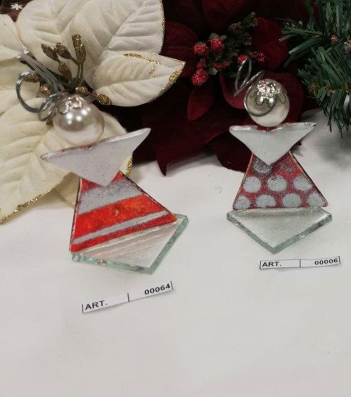 Due ornamenti in vetro a forma di angelo, uno a strisce rosse e uno a pois rossi, su una superficie bianca con stelle di Natale.