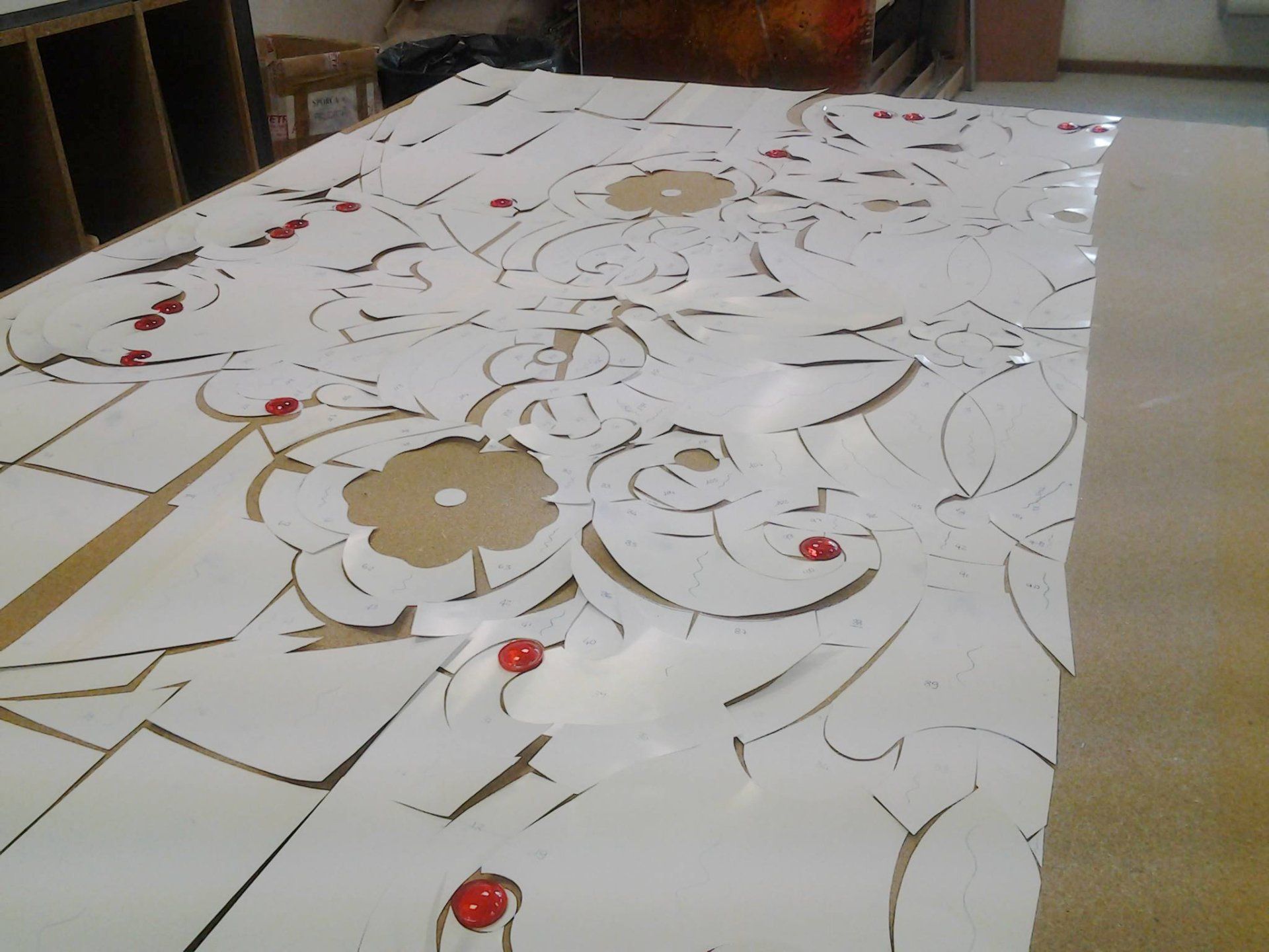 Foglio di carta bianco con motivi floreali ritagliati e dettagli rossi, disposto su un tavolo di legno in un laboratorio.