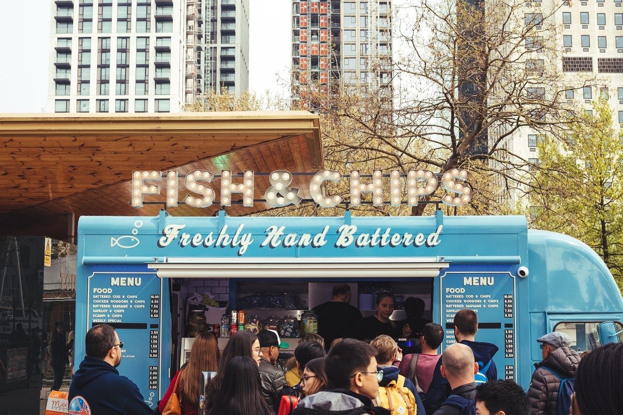 A group of people are standing outside of a fish and chips truck.