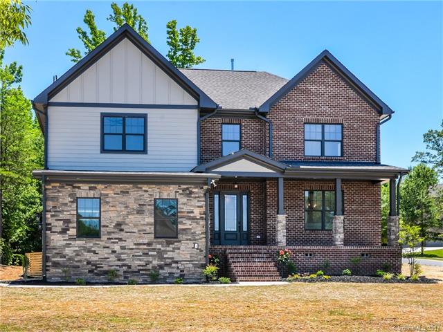 Two-story house with brick and stone facade, porch, and gabled roof against a blue sky.