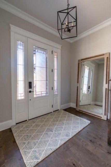 Elegant entryway with white door, rug, large mirror, and dark wood floors.