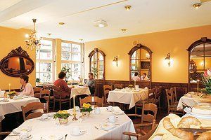Comedor acogedor de un restaurante con manteles blancos, ventanas arqueadas y algunos comensales sentados.