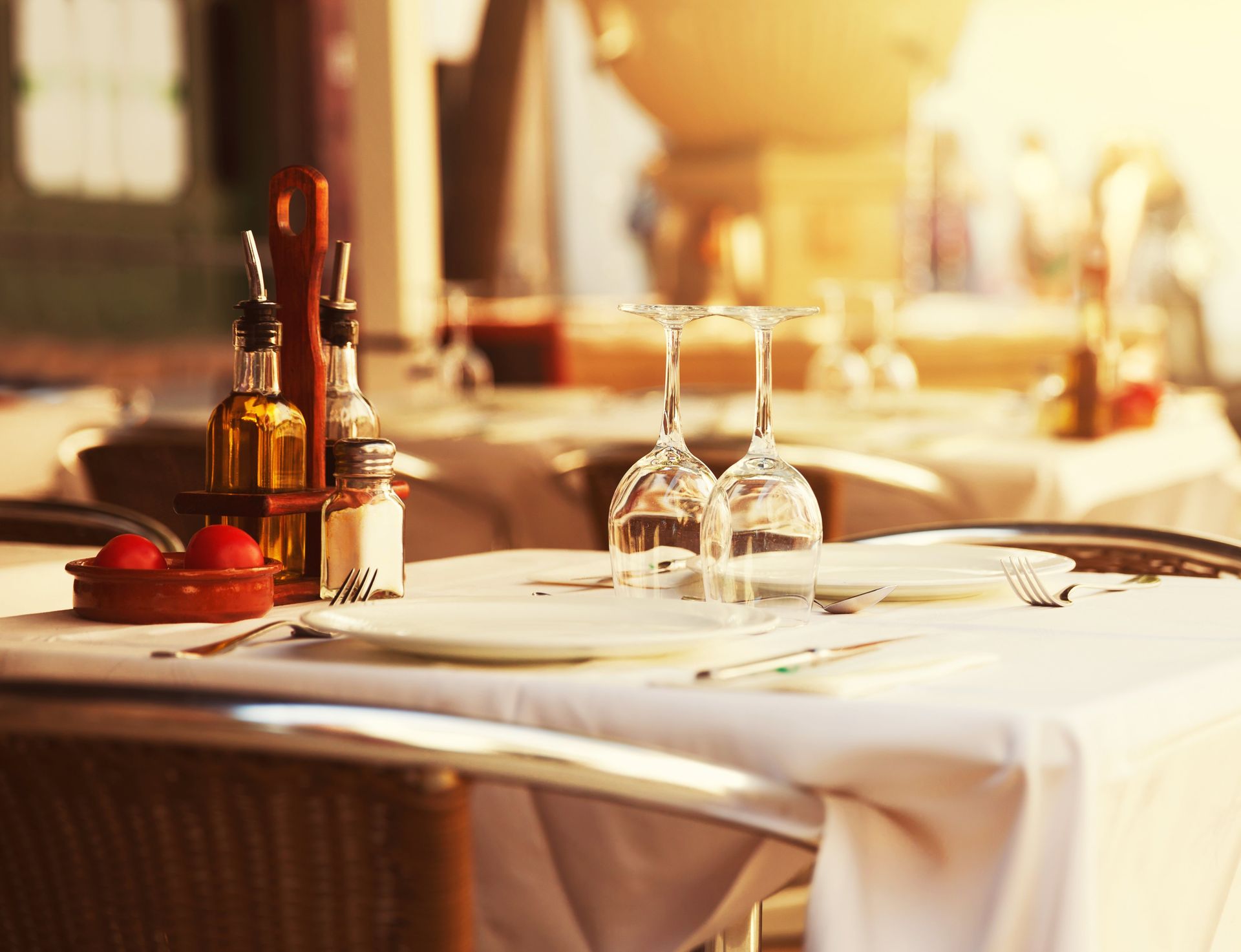 Élégante table de restaurant avec nappe blanche, verres à vin, bouteilles et fruits dans une lumière chaleureuse