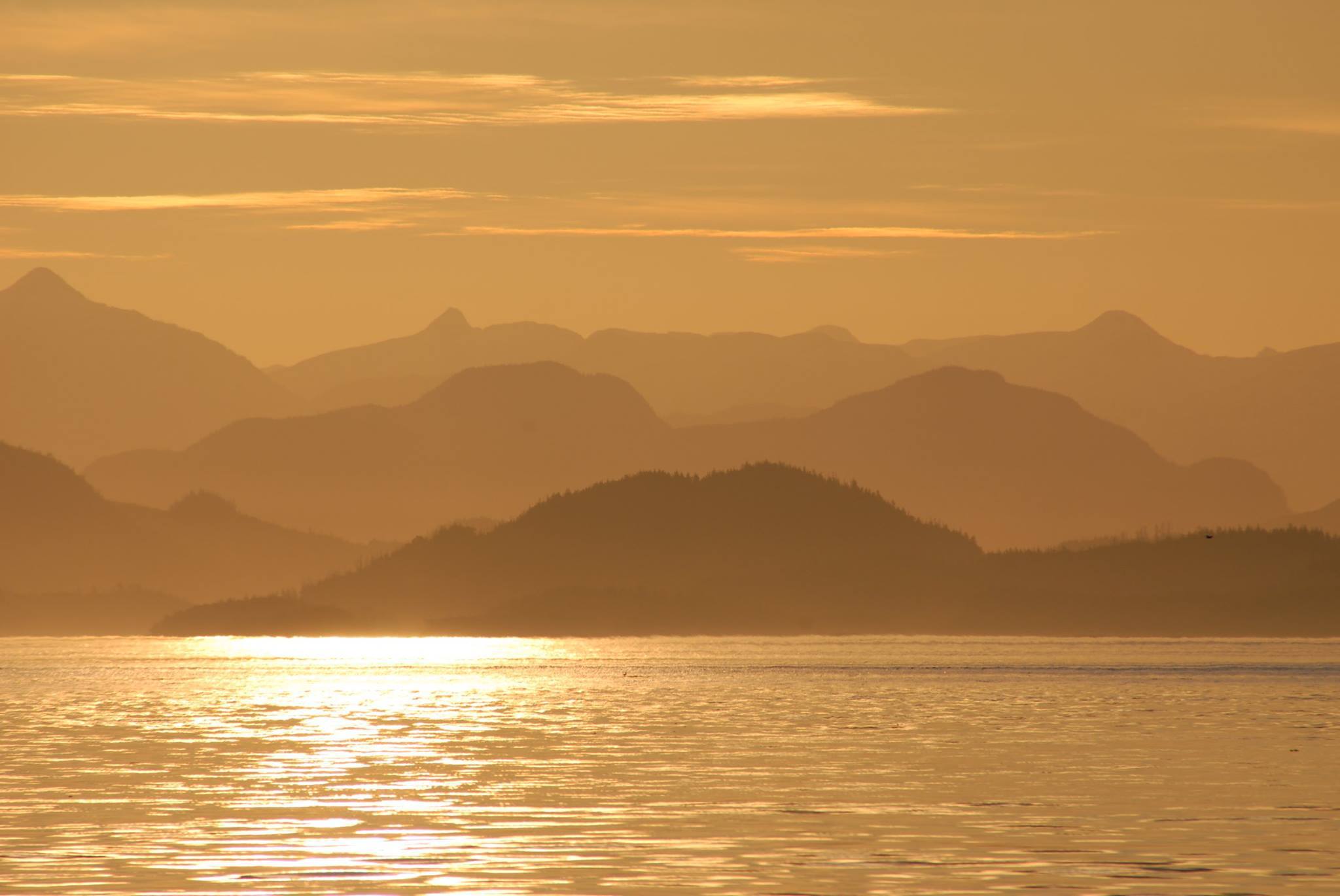 Golden sunset over calm water with silhouetted mountains in the distance.
