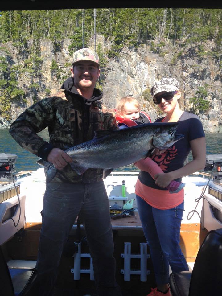 Two people on a boat holding a large fish, with a rocky riverbank in the background.