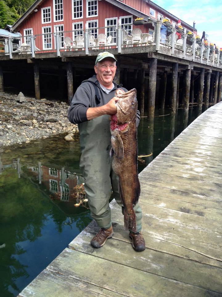 Man holding a large fish on a dock beside colorful waterfront buildings and calm water