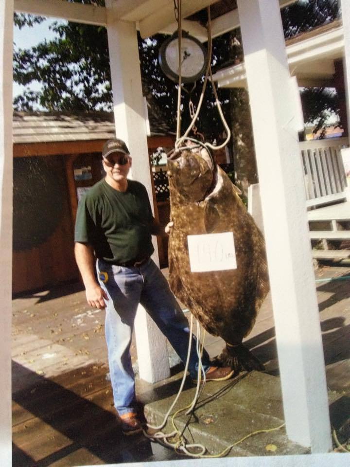 Man standing beside a hanging bear pelt display outdoors, holding ropes under a white pavilion.