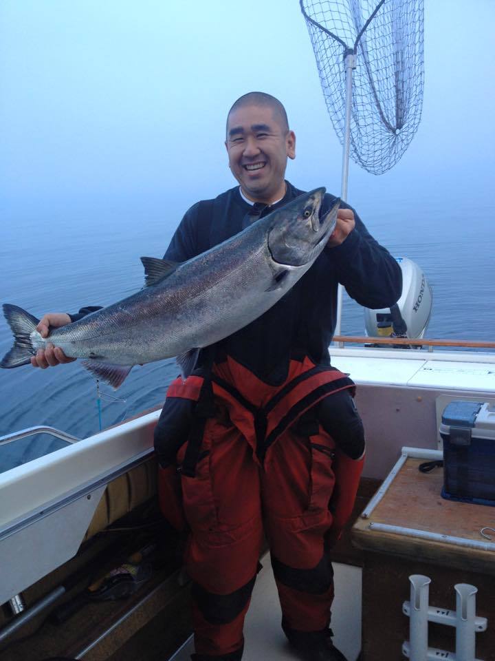 Smiling fisherman on a boat holding a large fish over the deck at sea