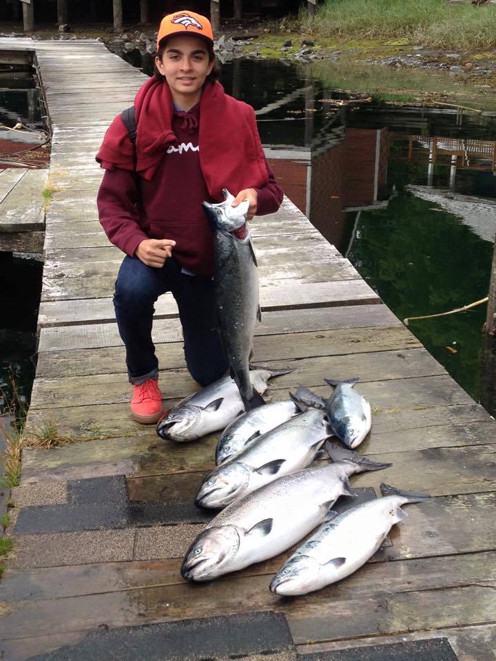 Person kneeling on a dock, holding a large fish beside several freshly caught fish.